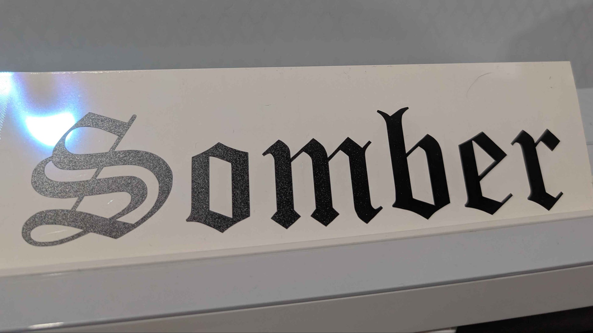 Sticker with 'Somber' text on a reflective surface